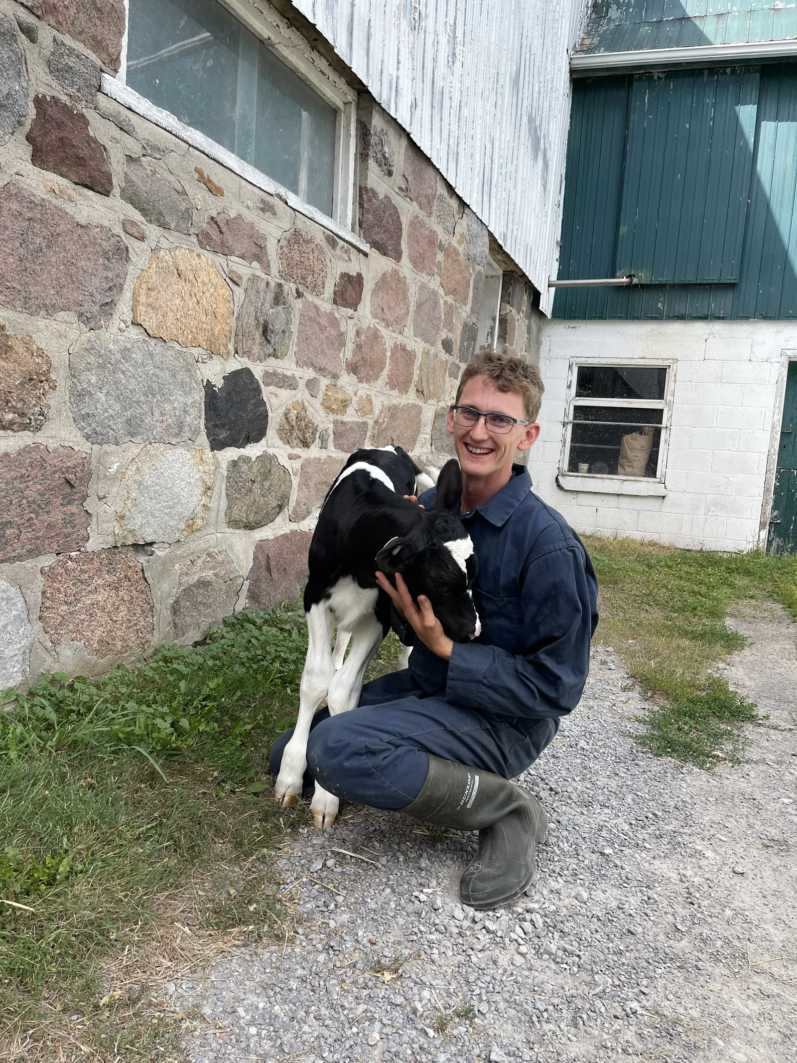 Thomas Zekveld smiling while holding a calf beside a stone barn